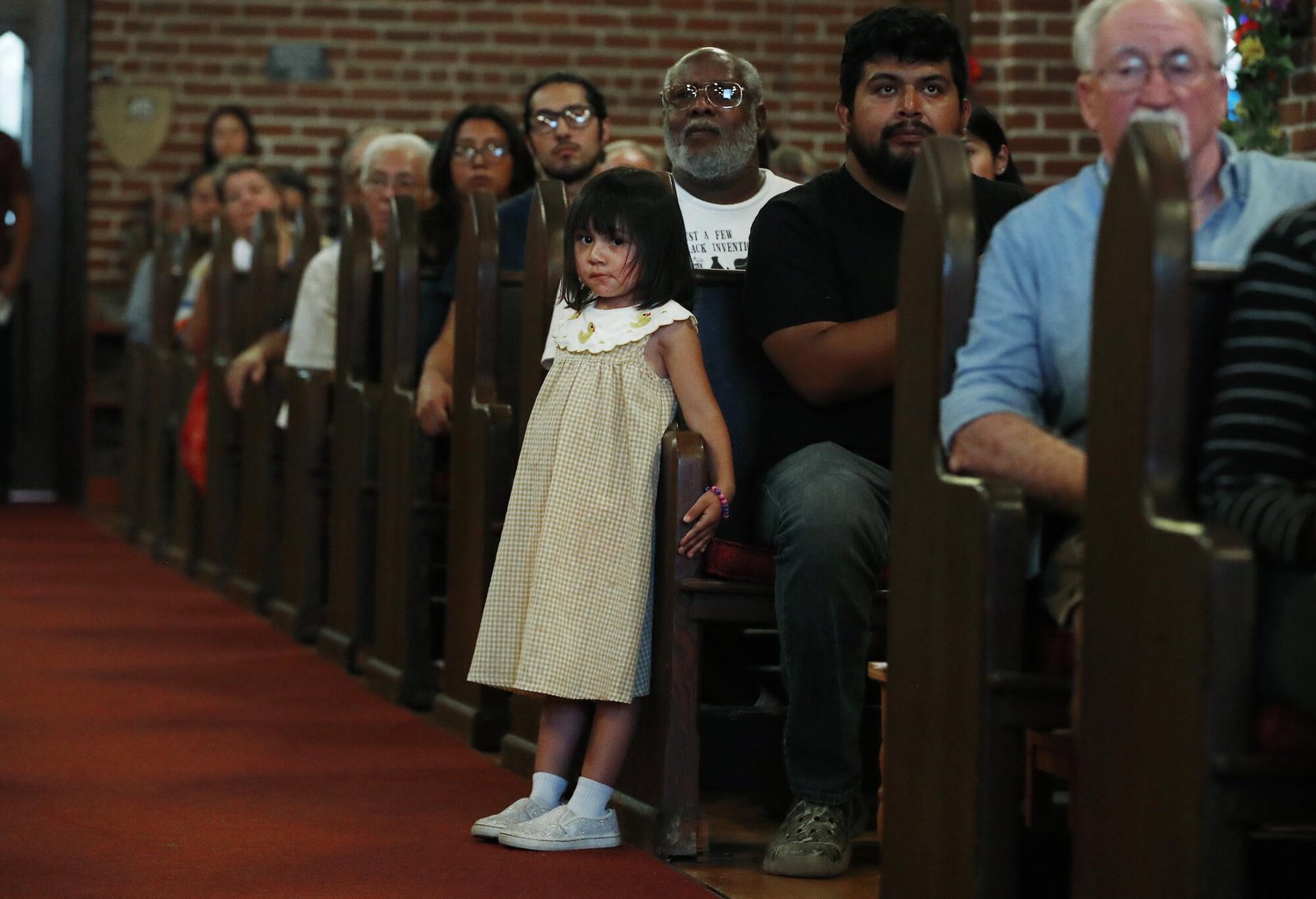 Una niña estaba junto a su padre, sentada en un banco de la iglesia con otras personas.