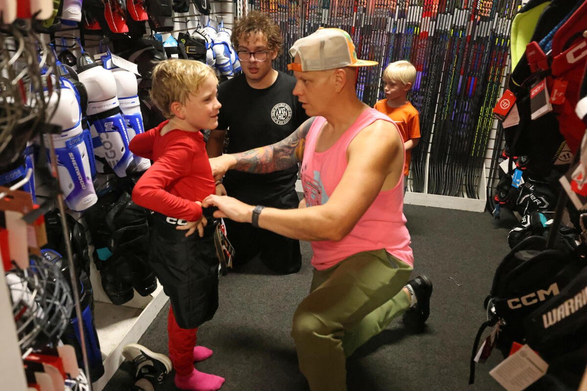 Sean Zabriskie, centro, ayuda a su hijo Connor, de 7 años, a probarse unos pantalones de hockey.