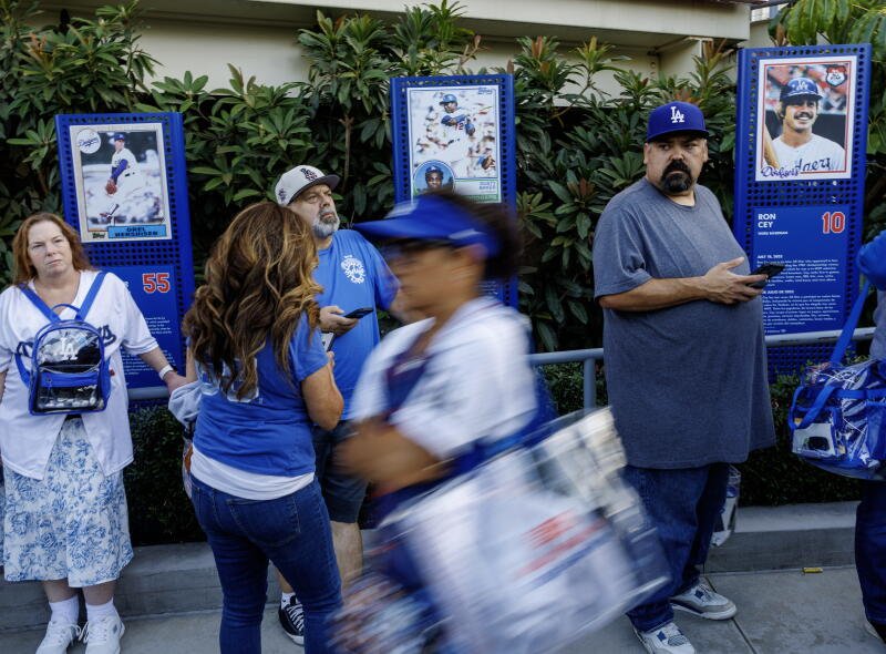 Los fanáticos de los Dodgers caminan entre plantas vívidas detrás de fotografías de ex Dodgers.