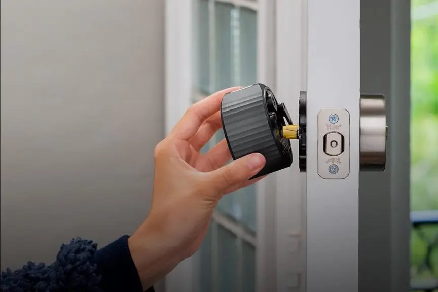 Sostenga con una mano el August Home Smart Lock 4 montado en la puerta blanca.