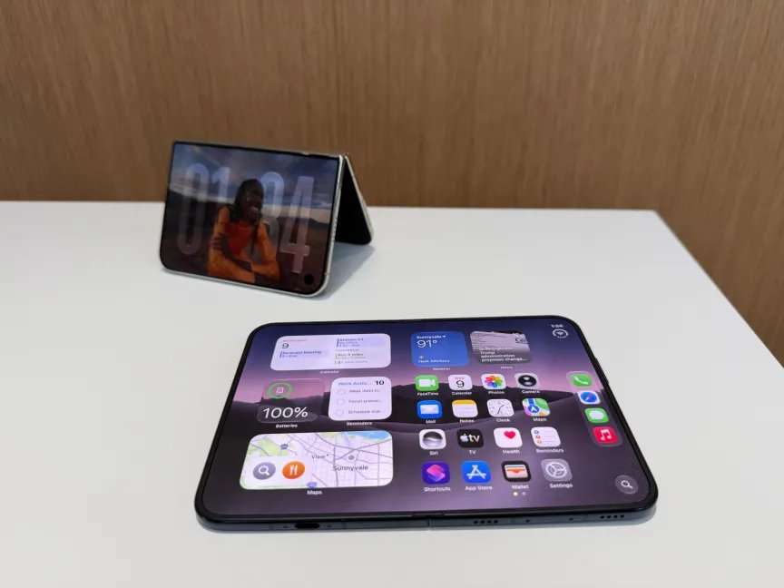 Hay dos teléfonos plegables sobre la mesa, uno desplegado y otro medio doblado y en posición vertical como una tienda de campaña.