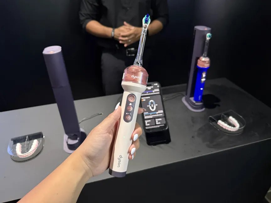 Una mano sostiene un cepillo de dientes Dyson CameraJet rosa.
