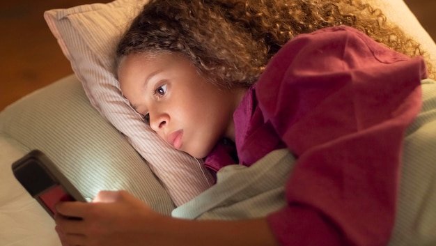 Lectura en la era digital l Fuente: https://img.freepik.com/free-photo/side-view-beautiful-young-girl-lying-bed-with-her-phone-curly-girl-playing-smart-phone-holding-it-one-hand-moving-finger-screen-family- concepto-de-ocio-infantil-utilizando-dispositivos-digitales_74855-22343.jpg?t=st=1722926456~exp=17 22930056~hmac=4d77333604a447d4338d481d65f2aa53f7f24aa950cce6941100bdb21de615e0&w=1060
