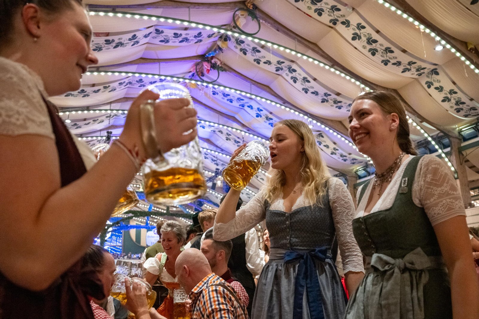 Tres mujeres se paran en un banco en Pschorr Braurosl Festzelt y beben cerveza.
