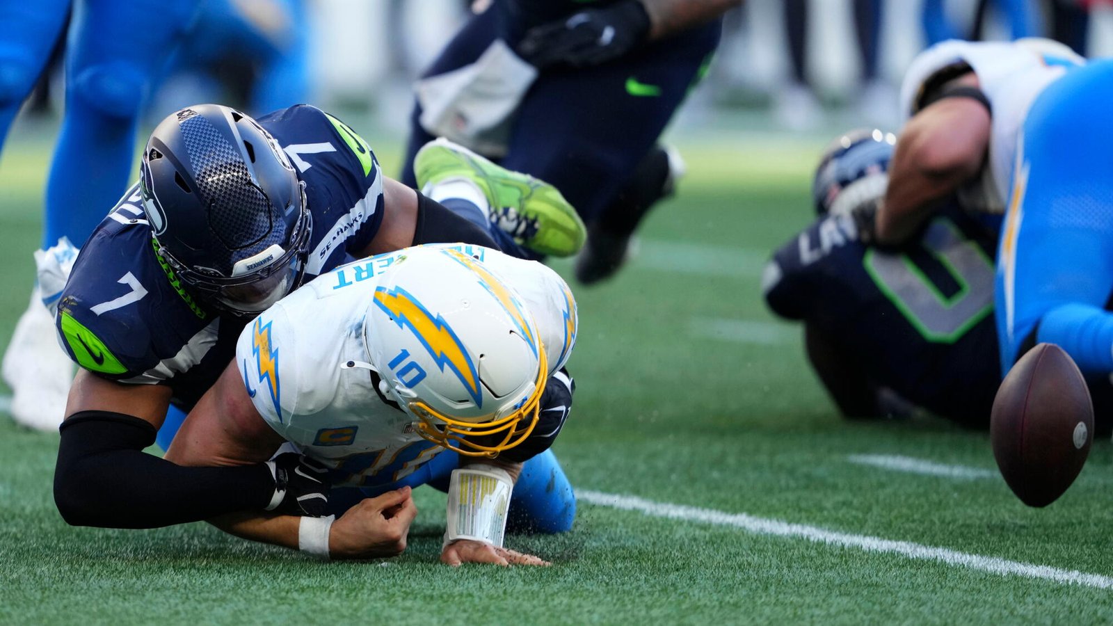 El mariscal de campo de los Chargers, Justin Herbert, pierde el balón cuando es tacleado por el apoyador de los Seattle Seahawks, Uchenna Nwosu.