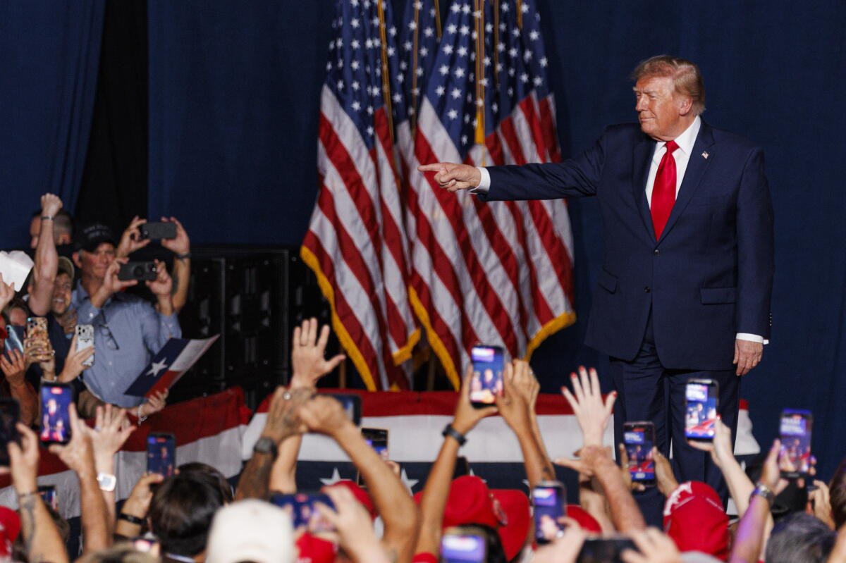 El presidente Trump señala a los fanáticos mientras caminaba hacia el escenario con la bandera de Estados Unidos detrás de él.