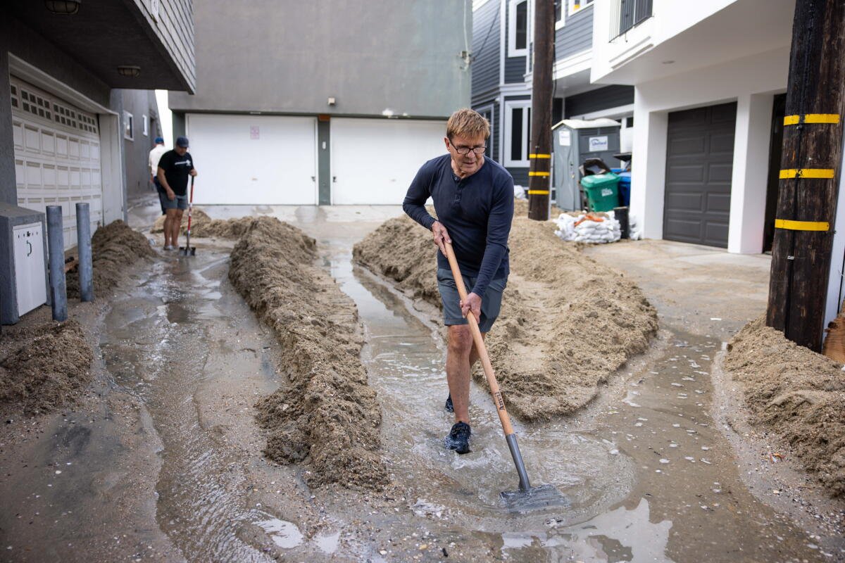 Robert Martin cava un camino de arena para mantener el flujo de agua en la Península de Long Beach el domingo.