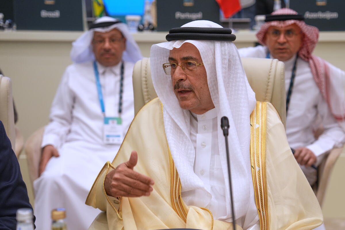 Un hombre saudita bien vestido se sienta con otros. Él está hablando y hay un micrófono frente a él. 