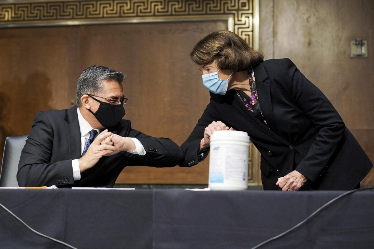 Xavier Becerra se codea con Dianne Feinstein, ambos con máscaras. 