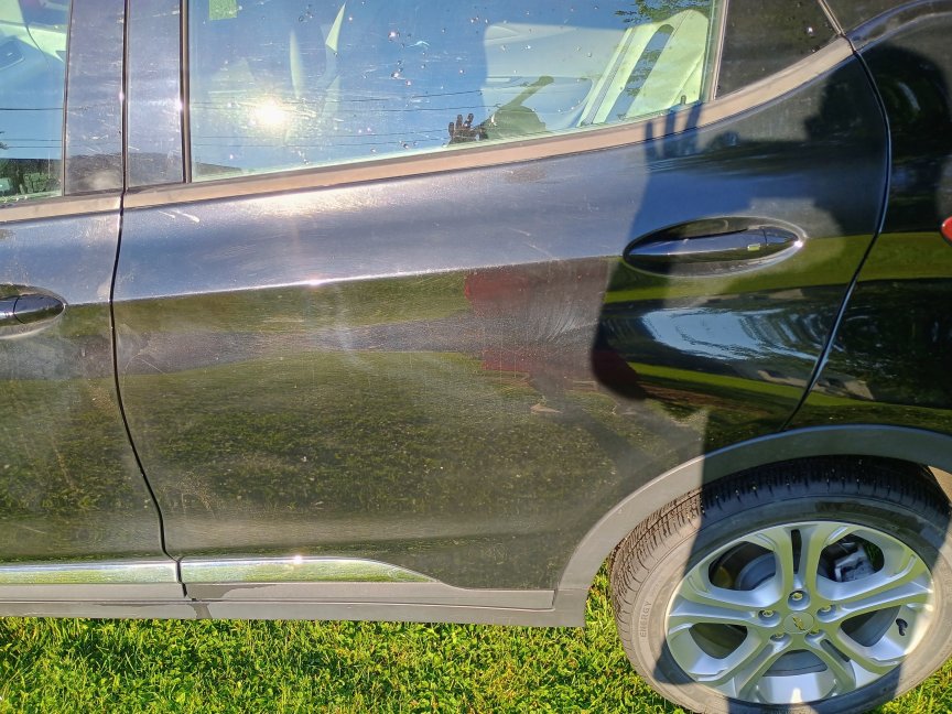 Puerta trasera del lado del conductor de un automóvil negro limpiada con LawnMaster LT506-2000A. Todavía tiene algunas manchas de barro notables, pero por lo demás está bastante limpio.