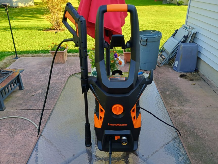 La lavadora a presión LawnMaster LT506-2000A negra y naranja viene completamente ensamblada sobre la mesa de vidrio del patio.