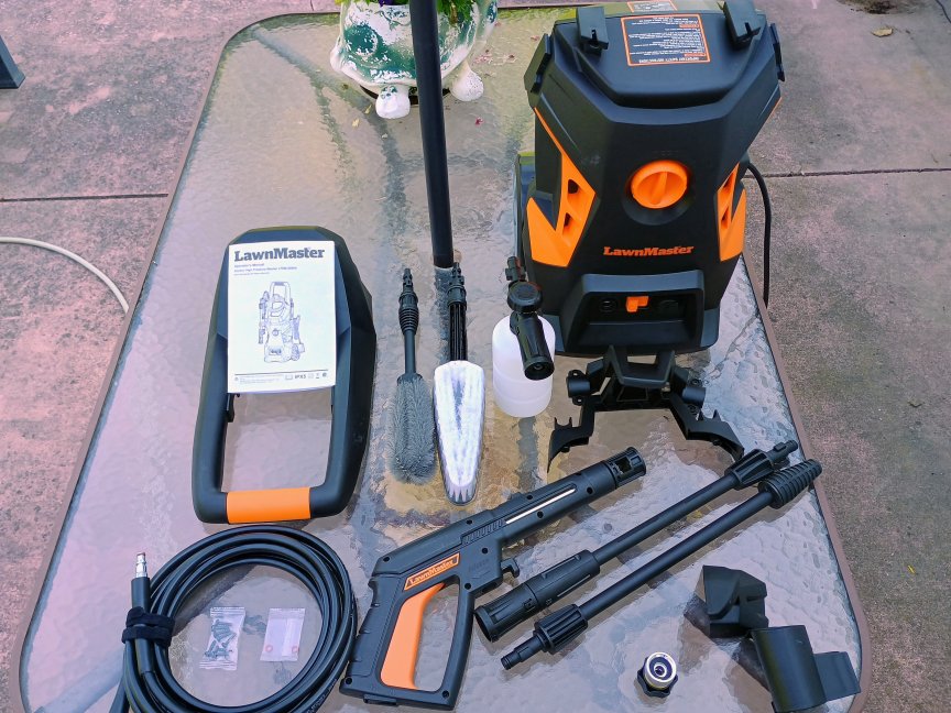 La lavadora a presión LawnMaster LT506-2000A y todos los accesorios que la acompañan se encuentran sobre una mesa de vidrio.